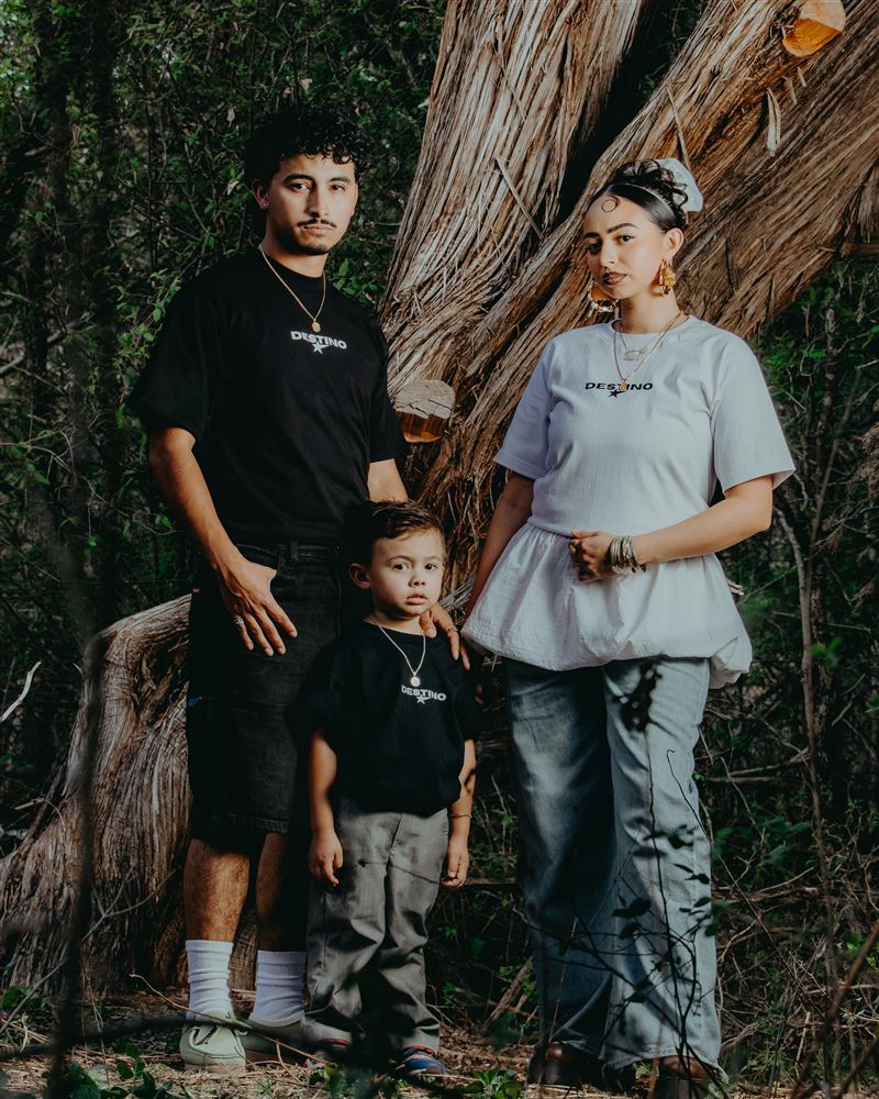 Family of three in Destino tees in front of a split cedar trunk