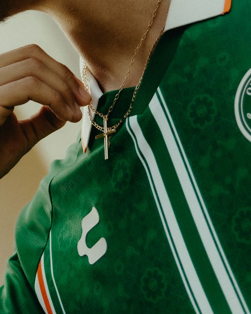 Close-up of a hand at the collar of the green Charly jersey with a gold cross necklace